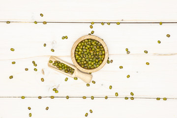 Lot of whole dry green mung beans with wooden bowl flatlay on white wood