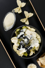 Pasta "butterfly" with white sauce Bechamel. Parmigiano cheese in rough paper on a black table. Italian food. Top view