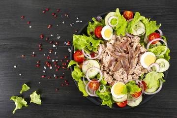Salad with tuna, anchovies and vegetables. Mediterranean food. The background is black. Top view. Copy space. Horizontal shot.