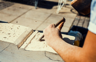 A stonemason is working on a sandstone block with chisel and hammer