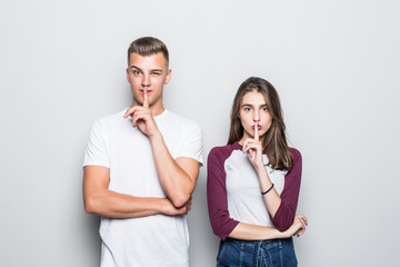 Portrait of a smiling couple showing peace gesture and looking at camera over gray wall