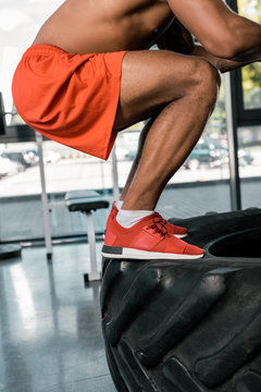 cropped image of african american athlete exercising on tire at gym