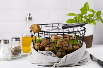 Baked potatoes in a black basket. Knife and fork. Olive oil, salt, pepper, basil. The background is white. Copy space. Horizontal shot.
