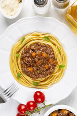 Pasta with Bolognese sauce. In a white plate. Parmesan cheese, a branch of tomatoes, olive oil and a fork. The background is white. Italian food. Copy space. Top view. Vertical shot.