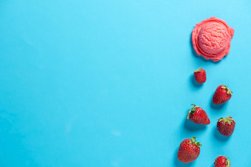 Top view of a pink icecream scoop and strawberries on a blue background