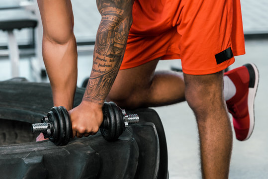 cropped image of tattooed african american sportsman exercising with dumbbell at gym