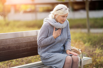 Senior Woman Suffering From Chest Pain While Sitting On Bench
