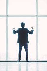 Fototapeta na wymiar Young successful businessman with raised arms in front of the city on panoramic windows