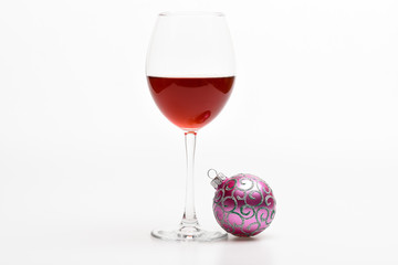 Winter holidays concept. Wineglass with red liquid or wine and christmas ball ornament isolated on white background. Winter celebration with alcohol drink. Glass with wine and christmas decoration