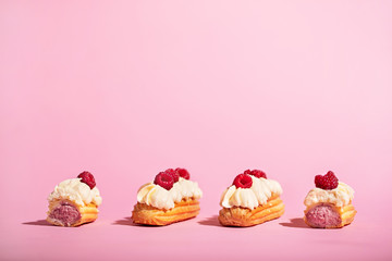 Four colorful eclairs with raspberries on pink background.