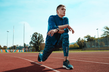 The fit male runner stretching legs preparing for run during training at stadium tracks. The...