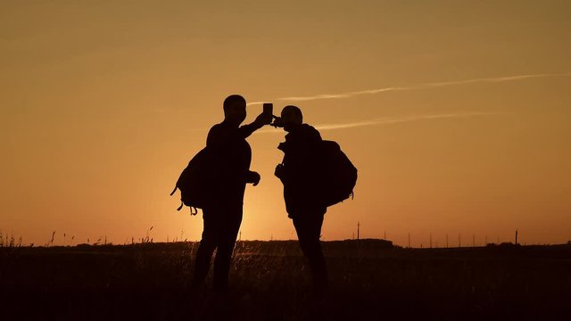 The silhouette of two man standing on the top of mountain with backpacks and use phone for navigation. Lifestyle, travel concept. Always online.