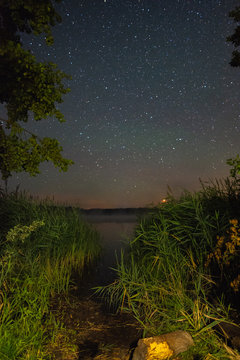 View of the lake among the trees at night . The milky way over the lake and lied .