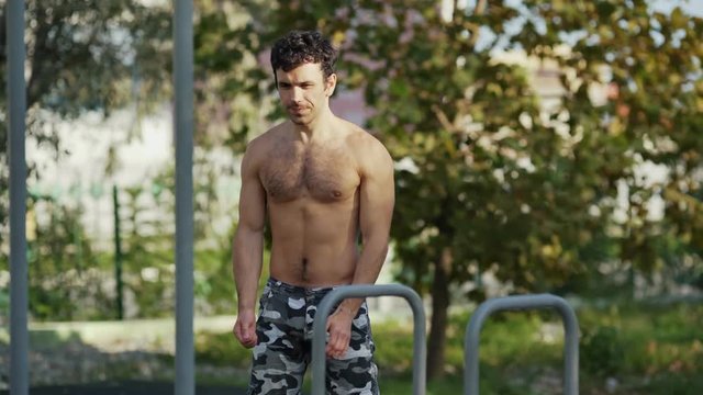 The athlete on the sports ground warms up before training. Muscular man goes in for sports in the open air. The guy in army pants does the exercises. Concept workout, crossfit, fitness, healthy.