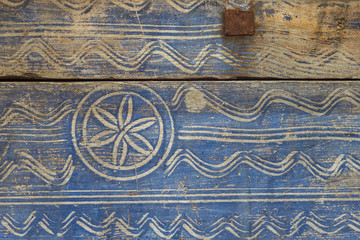 Old wooden chest is painted with blue paint and decorated with white ornament. Close-up. Background