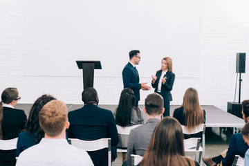 colleagues talking in front of multicultural audience during seminar in conference hall