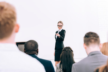 attractive lecturer pointing on multicultural audience during seminar in conference hall