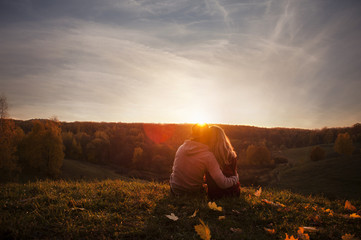 Very beautiful young couple in love guy with a girl sitting on the edge of a hill and watch the sunset outdoors