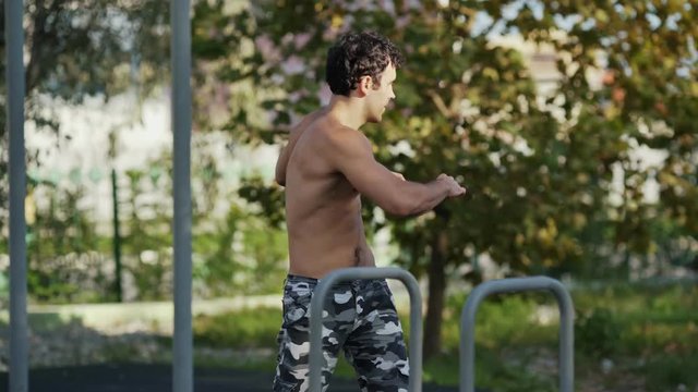 The athlete on the sports ground warms up before training. Muscular man goes in for sports in the open air. The guy in army pants does the exercises. Concept workout, crossfit, fitness, healthy.