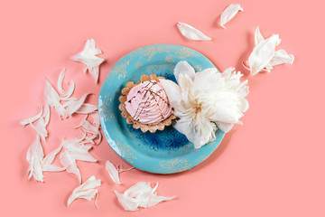 tartlett with cream on a blue plate with flower with petals of white pions, pink background. Flat lay. Copy space
