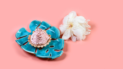 tartlett with pink cream on a blue plate with flower white pion, pink background. Flat lay. Copy space