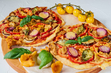 Veggie pizza with wild mushrooms,  vegetables and spices on the concrete background. Vegetarian pizza decorated with fresh yellow cherry tomatoes on the white kitchen table. Side view