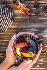 Woman holding glass with hot mulled wine on wooden background with  cookies and cinnamon. Vertical image. Top view.