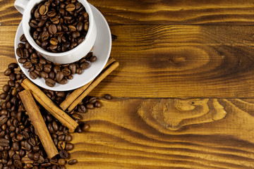 Coffee beans in white cup and cinnamon sticks on wooden table. Top view, copy space