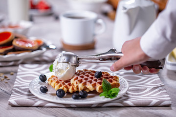 официант выкладывает шарик мороженого на бельгийские вафли