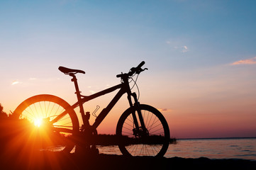 Beautiful close up scene of bicycle at sunset, sun on blue sky with vintage colors, silhouette of bike forward to sun