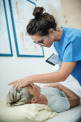 Sick woman lying down in bed and doctor checking temperature by putting hand on forehead.