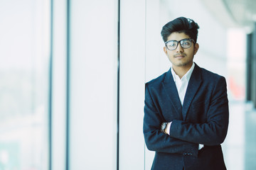 Portrait of a good looking smiling Indian businessman crossed arms standing at modern building