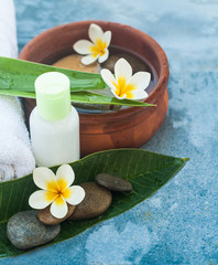 Obraz na płótnie Canvas Spa or wellness setting with tropical flowers, leaves and bowl of water with cream tube. Body care and spa concept on blue
