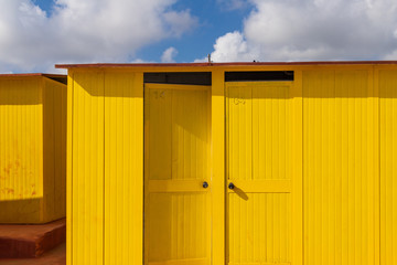 Beautiful yellow Bathing houses on sandy beach. Empty shelters on a sunny but moody day. Seaside architecture, colored paint, maze like labyrinth. Homelessness and lonely places.
