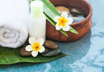 Spa or wellness setting with tropical flowers, bowl of water, towel and cream tube. Body care and spa concept on blue background