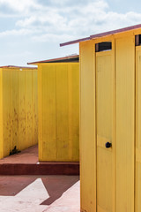 Beautiful yellow Bathing houses on sandy beach. Empty shelters on a sunny but moody day. Seaside architecture, colored paint, maze like labyrinth. Homelessness and lonely places.