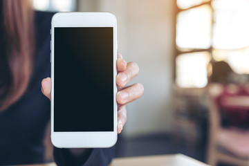 Mockup image of a woman holding and showing white mobile phone with blank screen in cafe