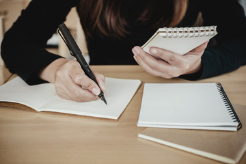 Fototapeta premium A woman holding and writing on notebook while sitting in cafe with blur green nature background