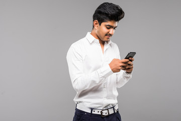 Young happy Indian Sikh man using mobile phone isolated against gray background