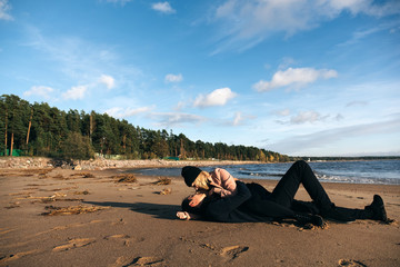 Young sexy sensual couple laying and hugging on sand at the beach. Passion between two lovers. Sex and love on the beach. Cold autumn weather, coastline, park and ocean on the background.