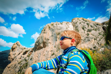 little boy with backpack hiking in mountains