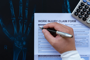 wrapped hand filling up a work injury claim form with a calculator on top of an X-ray film medical...