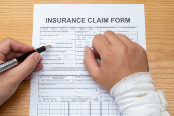 man with a wrapped hand filling up an insurance claim form medical and insurance concept no logo or...