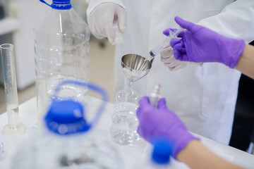 Close up of technologist`s and his asisstant hands pouring chemical with syringe into chemical balloon. Water quality check concept.