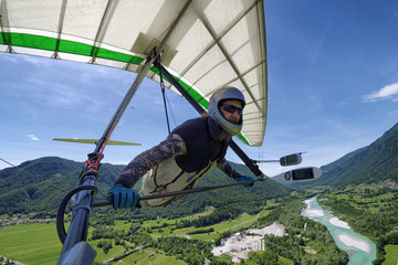 Selfie shot of brave extreme hang glider pilot soaring the thermal updrafts above alpine valley