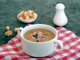 Yellow pea soup with smoked ham, pearl barley and carrots on a dark background. Served with white wheat bread croutons
