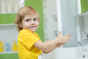 Fototapeta na wymiar little boy in a bathroom washes hand with soap