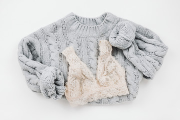 Flat lay of cozy knitted woman sweater and lace bralette on white
