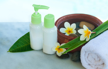 Obraz na płótnie Canvas Spa or wellness setting with tropical flowers, bowl of water with stones, towel and cream tube. Body care and spa concept