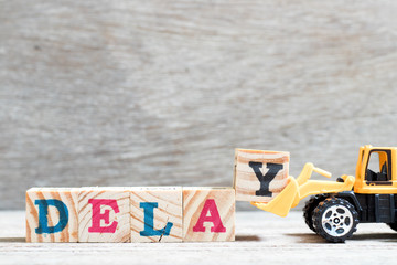 Toy bulldozer hold letter block y to complete word delay on wood background